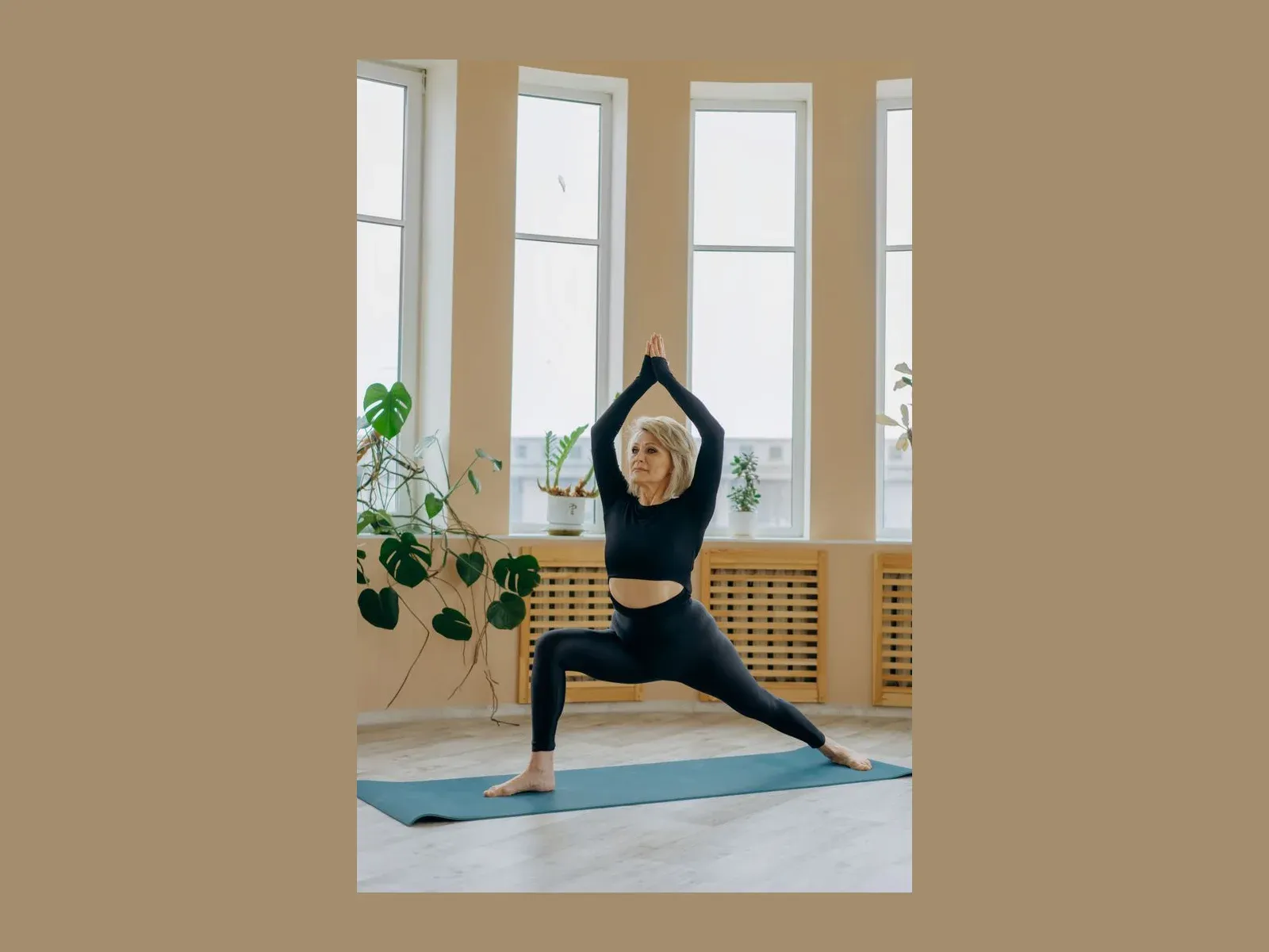 A woman in her sixties on a mat in a bright room, in a standing lunge with both arms stretched overhead
