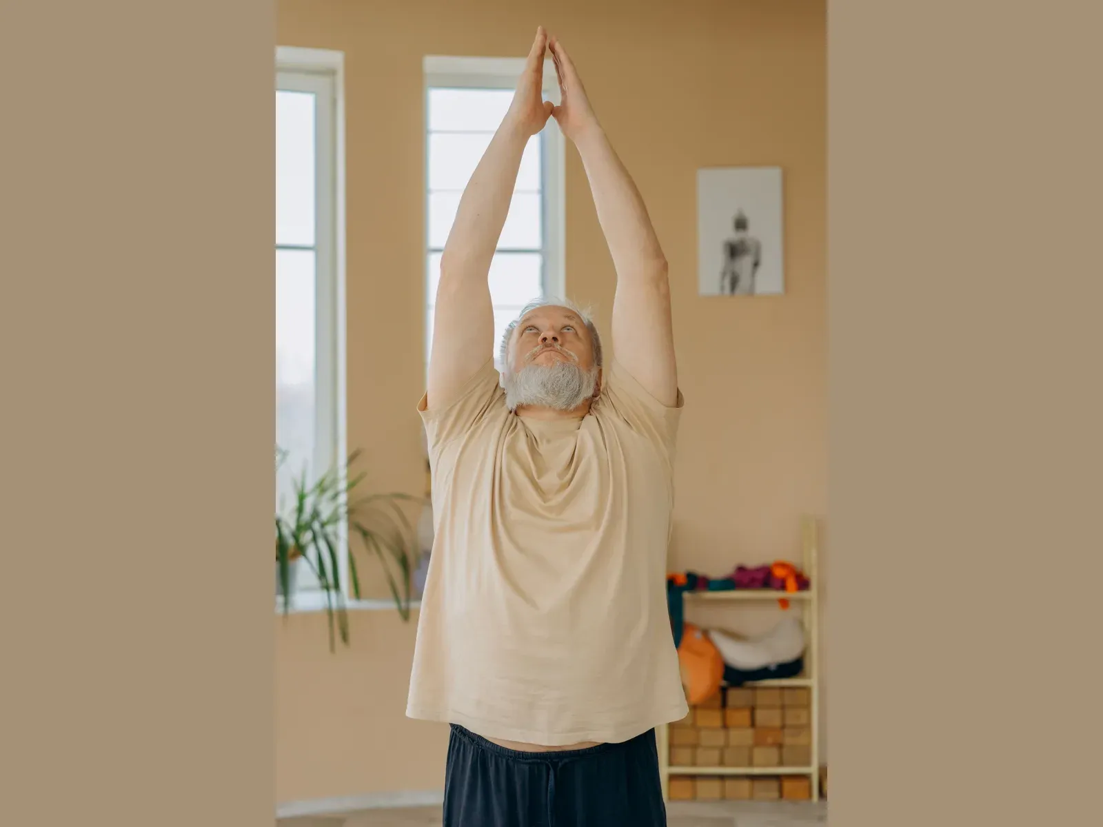 A man in his seventies standing tall in a balance exercise, both arms stretched overhead, palms together