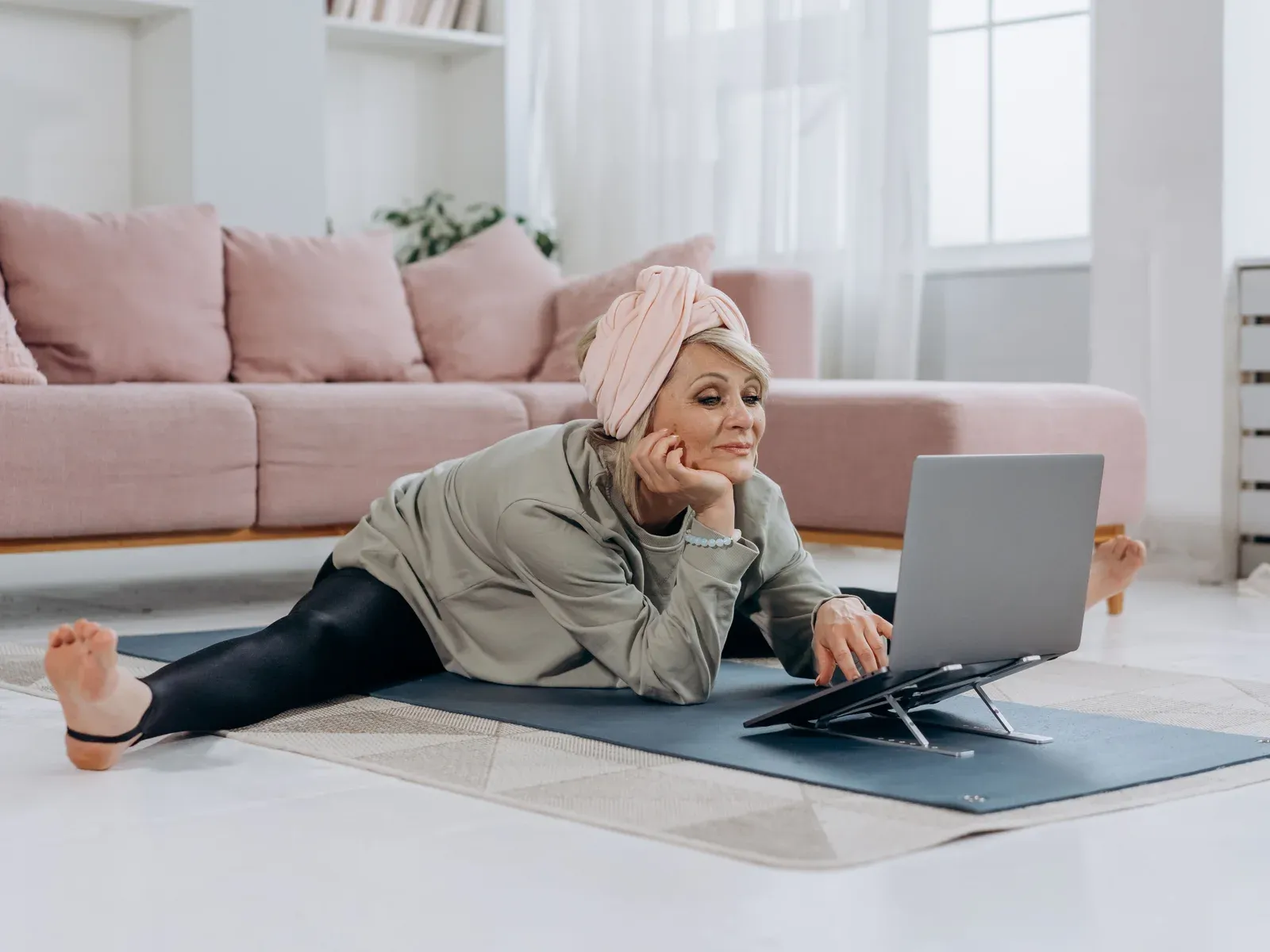 A woman on a mat in a wide straddle stretch, following a session on a laptop in front of her