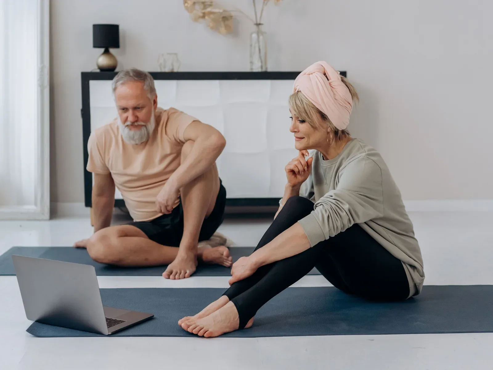 A couple in their sixties on mats at home, following an online training session on a laptop