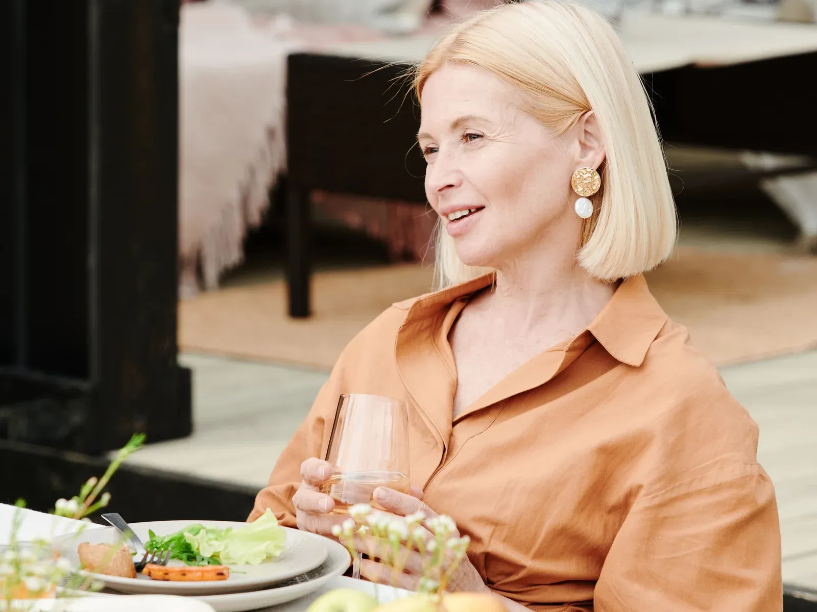 A woman in her fifties at an outdoor table with a plate of salad, fruit and a glass of water